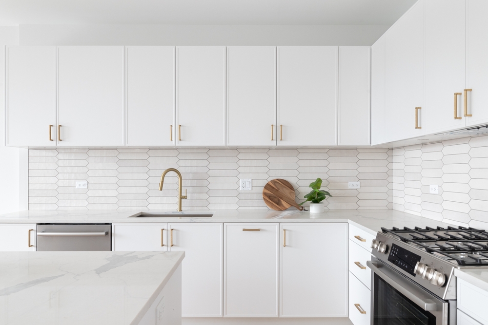 The Best Cabinet Layouts for Maximizing Storage and Style 1 A beautiful kitchen detail with white cabinets, a gold faucet, white marble countertops, and a brown picket ceramic tile backsplash.