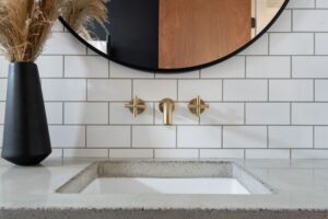 Bathroom photo of under mount sink with grey concrete countertop and classic white subway tiles with polished brass gold wall faucet